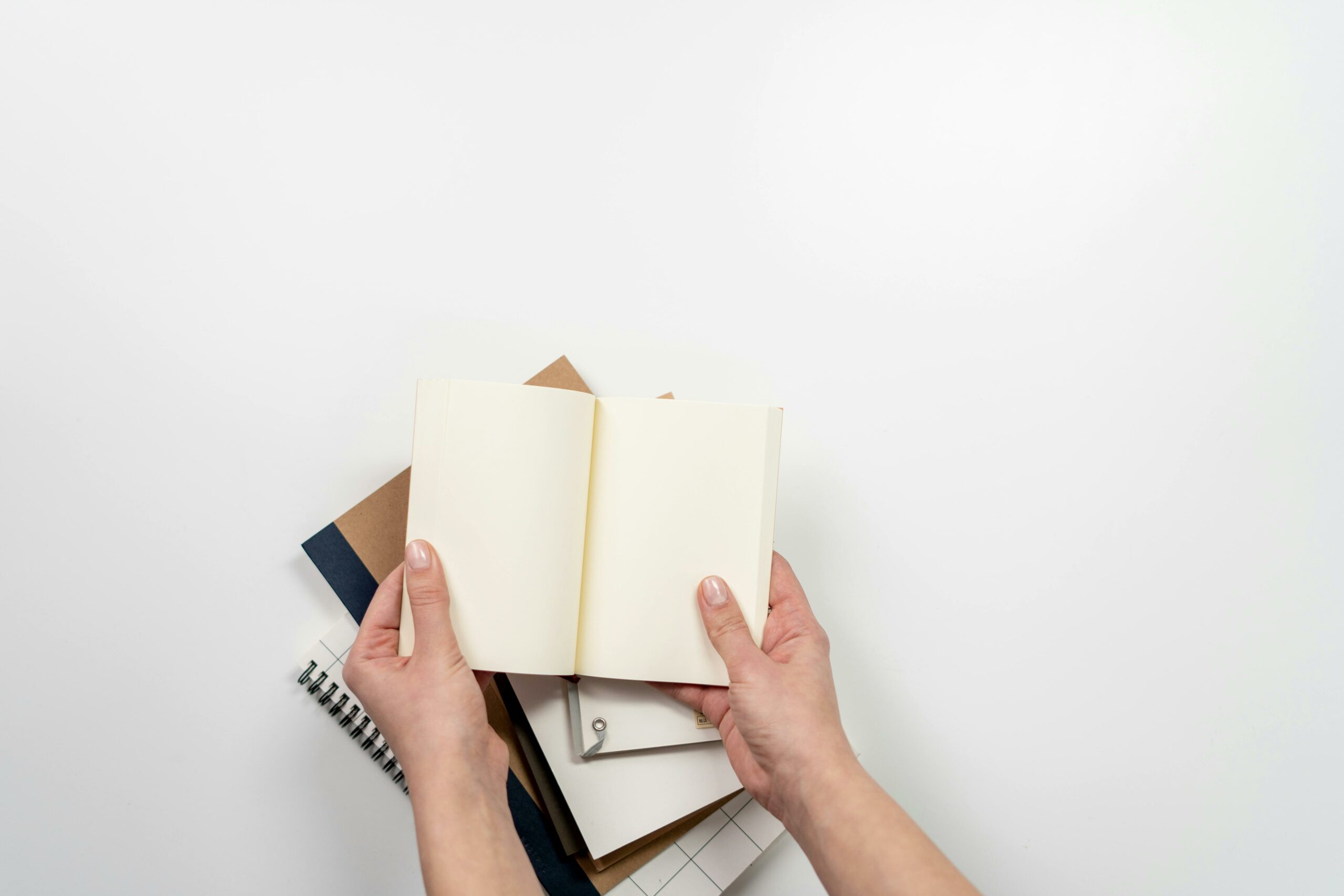 Hands holding an open blank notebook above a stack of stationery items on a desk, perfect for planning concepts.
